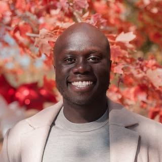 DJ Kadero smiling in a light jacket against red foliage